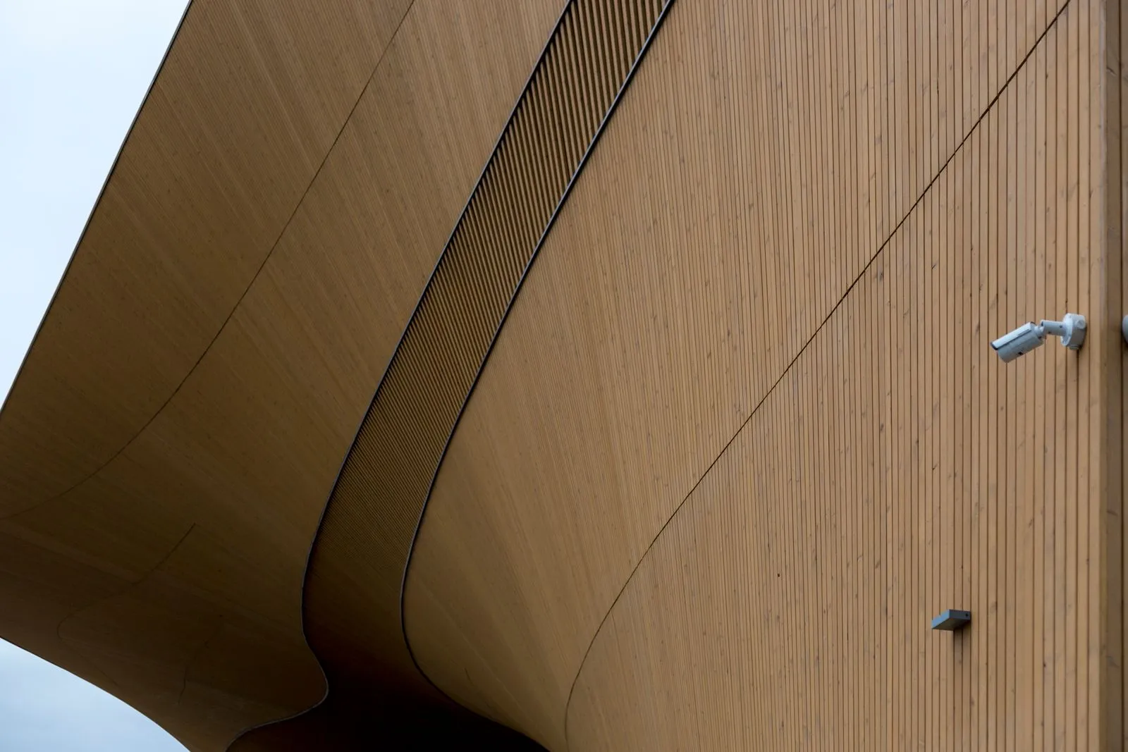 Curved wooden architecture with a surveillance camera attached for modern security. Aesthetic exterior design.